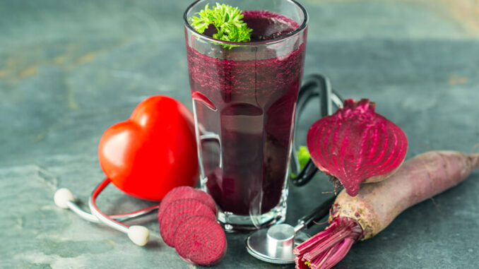 Ein mit Rote Beete Saft gefülltes Glas umgeben von Roter Beete und einem Stethoskop