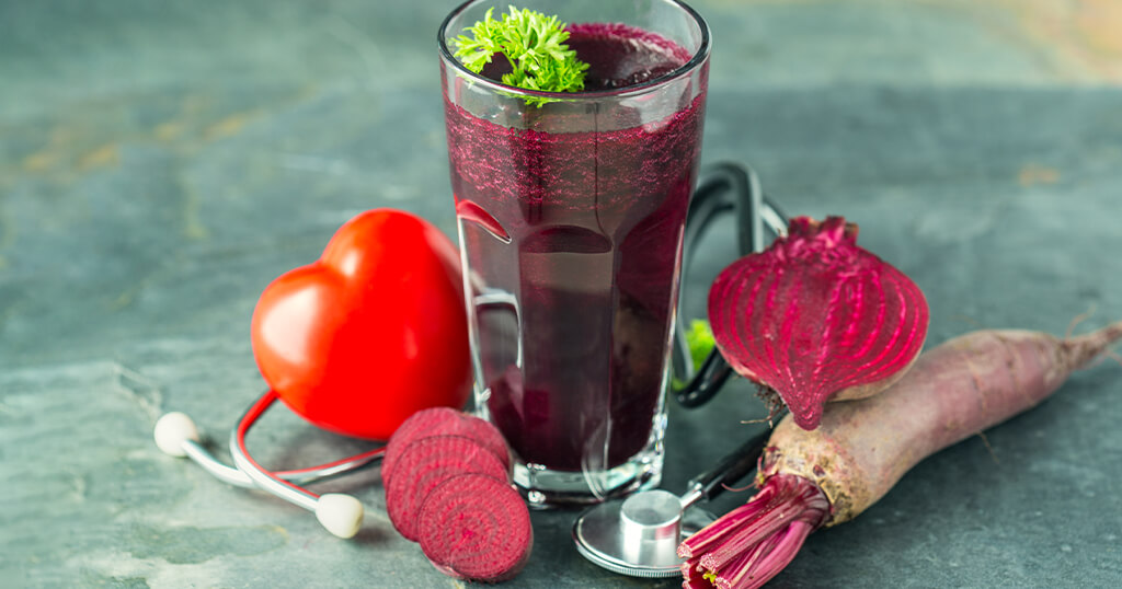 Ein mit Rote Beete Saft gefülltes Glas umgeben von Roter Beete und einem Stethoskop