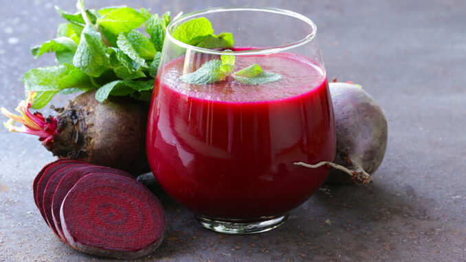 Ein kleines Glas gefüllt mit Roter Beete und oben mit Minze dekoriert und das Glas ist umgeben von Roter Beete