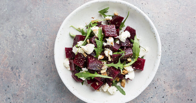 Ein bunter Salat mit Rote Beete Stückchen, Blumenkohl, Rucola und Nüssen serviert auf einem weißen Teller