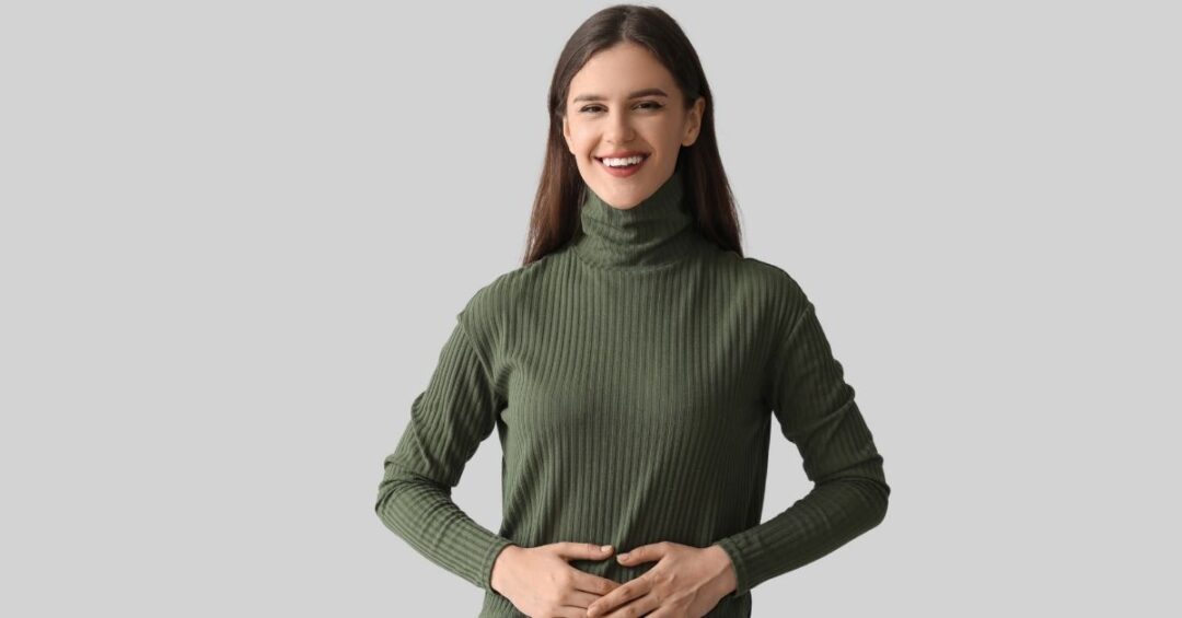 Lächelnde Frau hält die Hände auf den Bauch als Symbol für eine gesunde Verdauung und ein gutes Bauchgefühl.