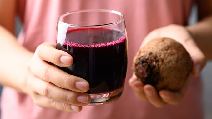 Frau hält ein Glas mit Rote-Beete-Saft und eine frische Knolle
