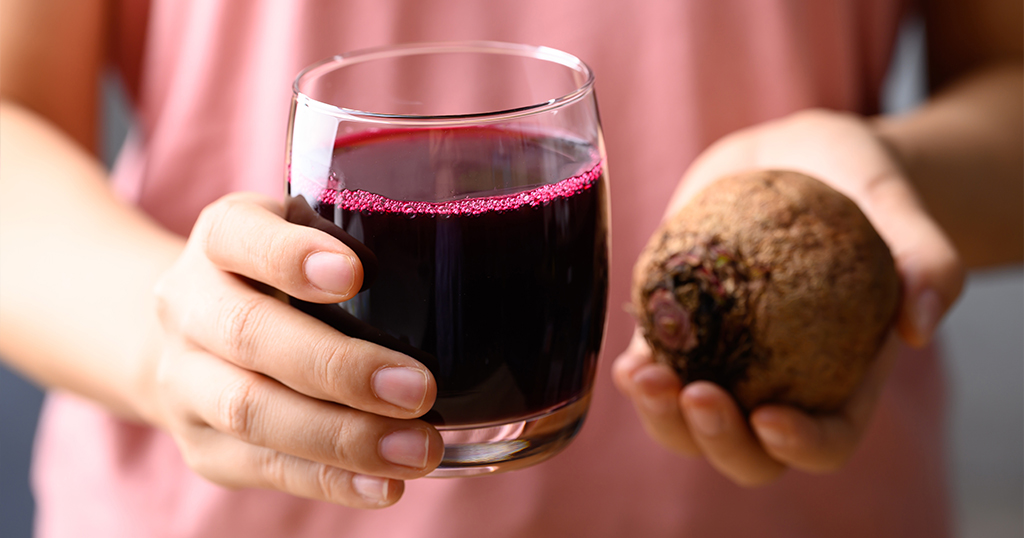 Frau hält ein Glas mit Rote-Beete-Saft und eine frische Knolle